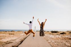 Joyful couple jumping with arms raised on way to seashore
