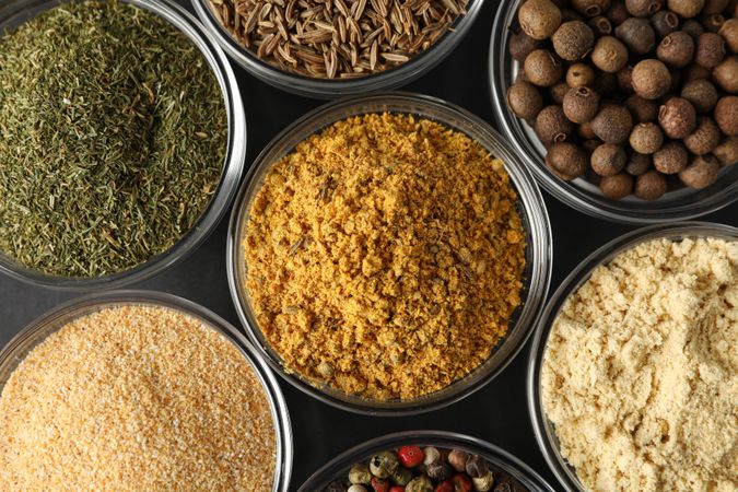 Close up top view of glass bowls full of spices arranged on dark table