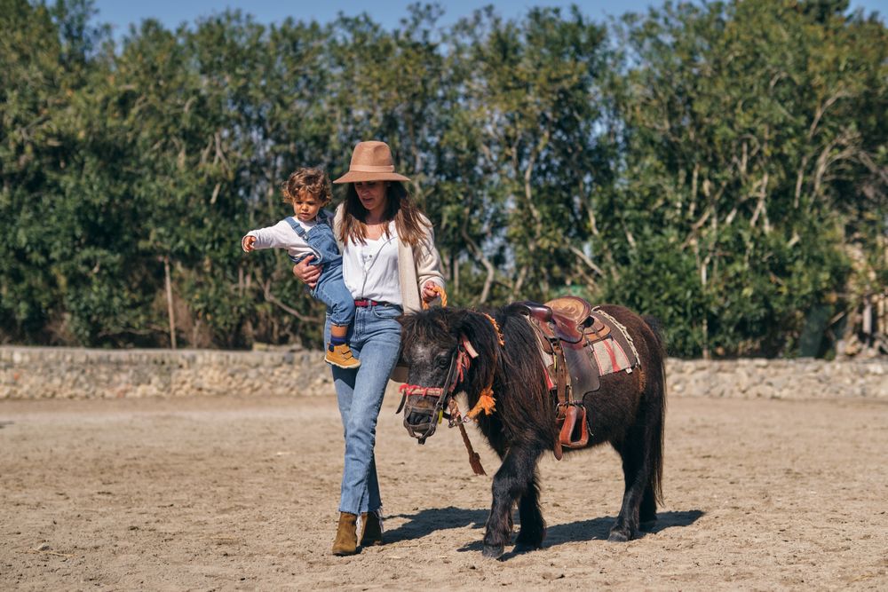 Young mother carrying child while walking in paddock with purebr