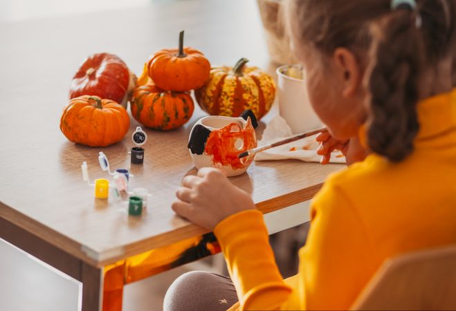 A little girl paints a clay hand made pumpkin. Halloween party. Crafts for children.