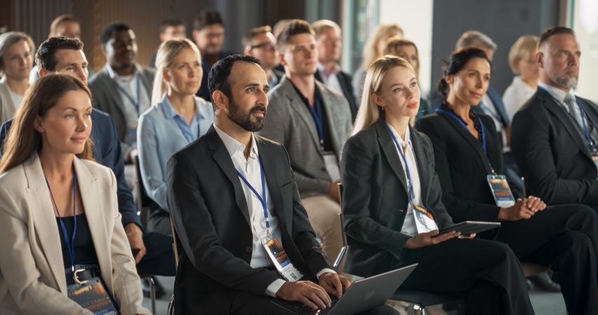 Diverse Biopharma Entrepreneurs Sitting In Crowd At International Medical Summit, Using Laptops, Tablets To Take Notes.