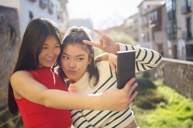 Happy female friends making peace sign and taking selfie on sunny day