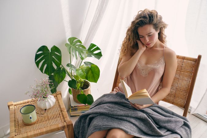 Young woman sitting on wicker chair with book