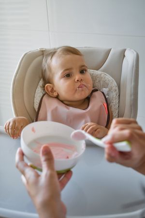 Crop person feeding daughter with spoon