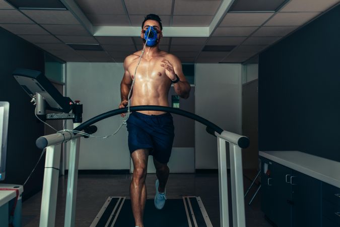 Fit young man running on treadmill with a mask in sports lab