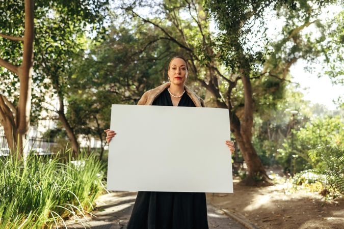 Stylish woman looking at the camera while holding up a blank placard