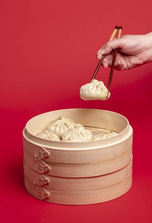 Woman hand taking chinese dumpling with wooden chopsticks