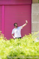 Man in headphones taking selfie with phone in front of pink wall 4A1xm4