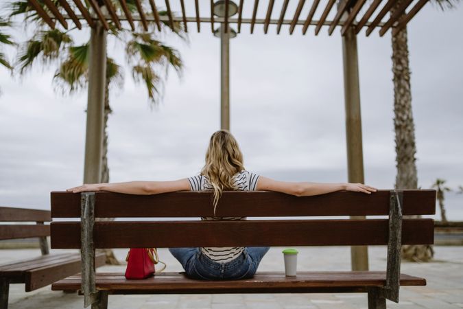 Anonymous woman with disposable cup of coffee sitting on street bench