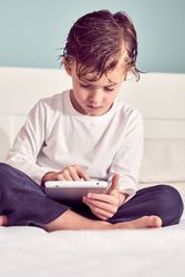 Serious boy browsing digital tablet on bed