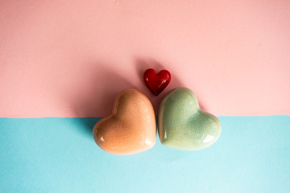 Orange, red and green heart ornaments on blue and pink pastel background 
