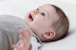 Happy baby girl lying on back over white bedcover.