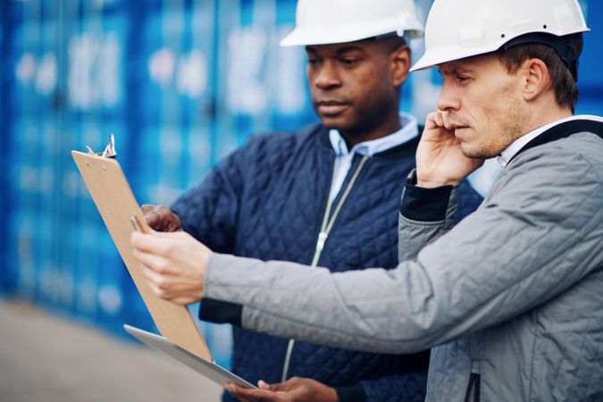 Two serious men in hard hats focused on a clipboard