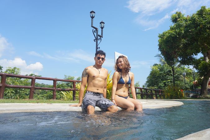 Man and woman in swimsuit sitting by the poolside