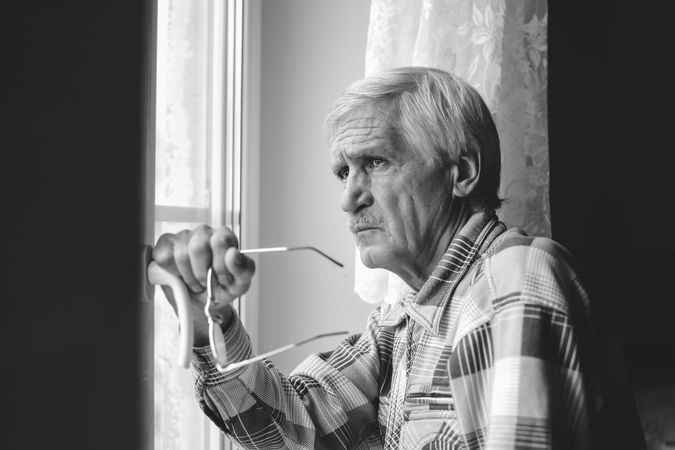 Grayscale photo of older man looking outside the window