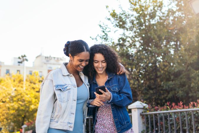 Black Latina friends using a smartphone in the park.