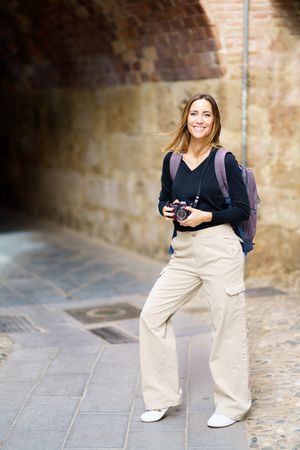 Happy woman with camera near arched passage in old town