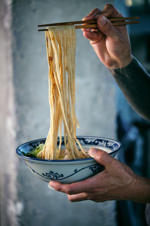 Crop man with noodles on chopsticks above tasty ramen
