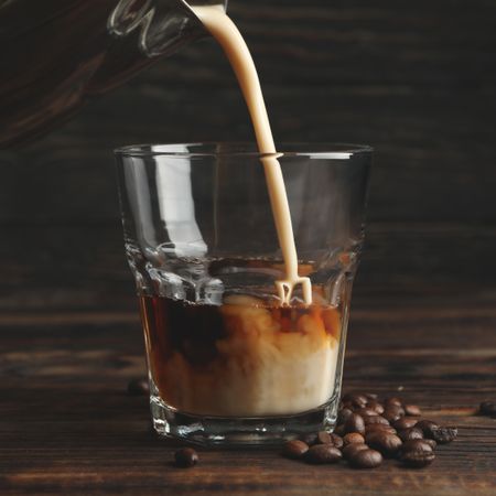 Milk is poured into a glass of coffee. Composition with ice coffee