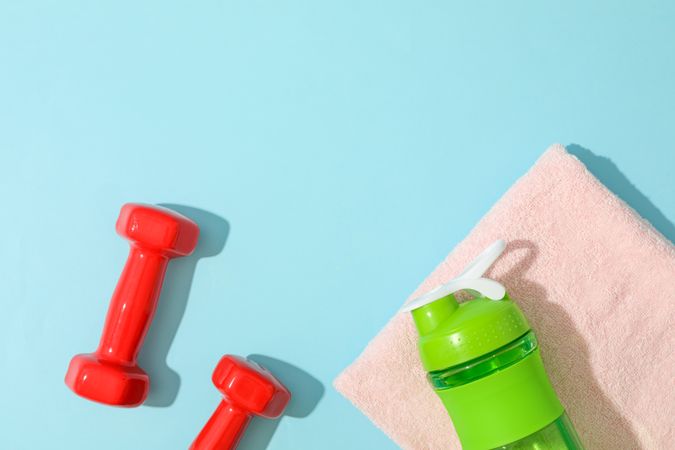 Flat lay composition with towel, dumbbells and fitness bottle on blue background
