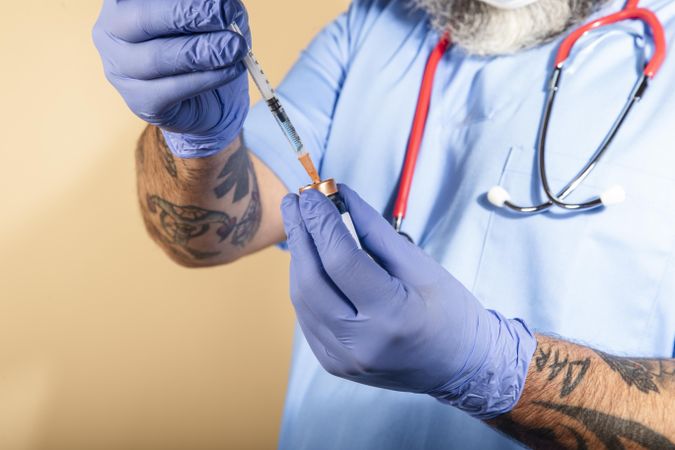 Tattooed healthcare worker with stethoscope on neck holding a syringe