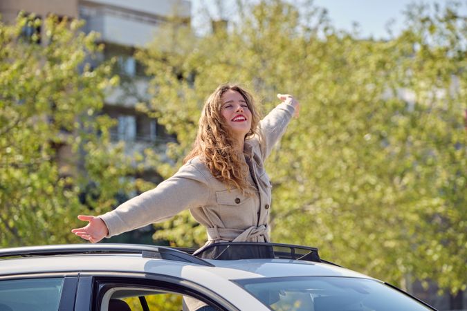Smiling woman standing in car sunroof with outstretched arms