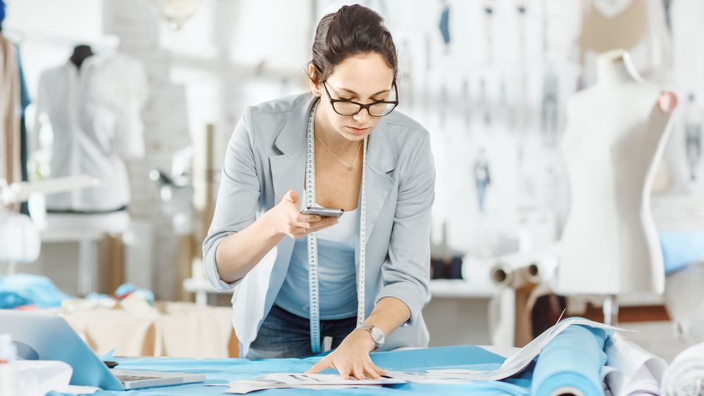 fashion, designer,  Stands at the Table, With Her Smartphone Takes Photos of Sketches.