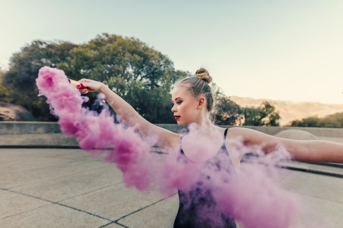 Young woman dancing outdoors with pink smoke bomb