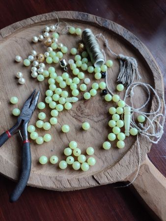 Green and pearly beads scattered on wooden board, along with strings and pliers