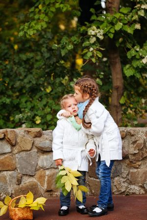 Big sister kissing her little sister in front of stone wall in park