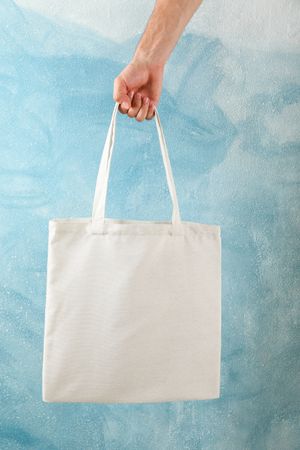 Male hand holding tote bag against blue background, copy space