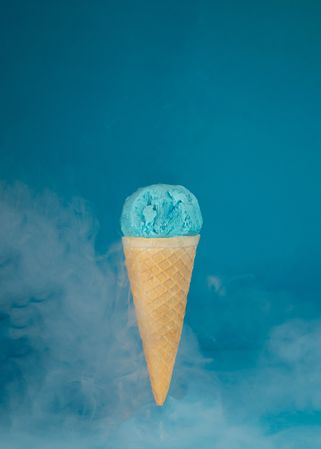 Blue ice cream in cone on blue background with smoke