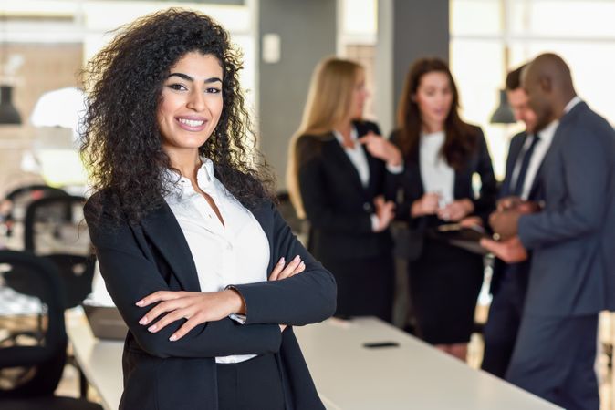 Curly haired business leader standing in foreground of busy office