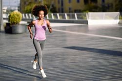 Woman with afro hairstyle running outside on pavement in city