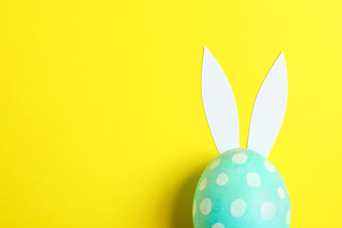 Decorated Easter egg with cute bunnies ears on yellow background. Space for text