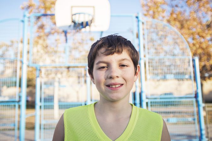 Portrait of a young teen male with sleeveless standing on a street basket court while smiling at camera