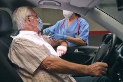 Unrecognizable nurse inoculating mature driver in car