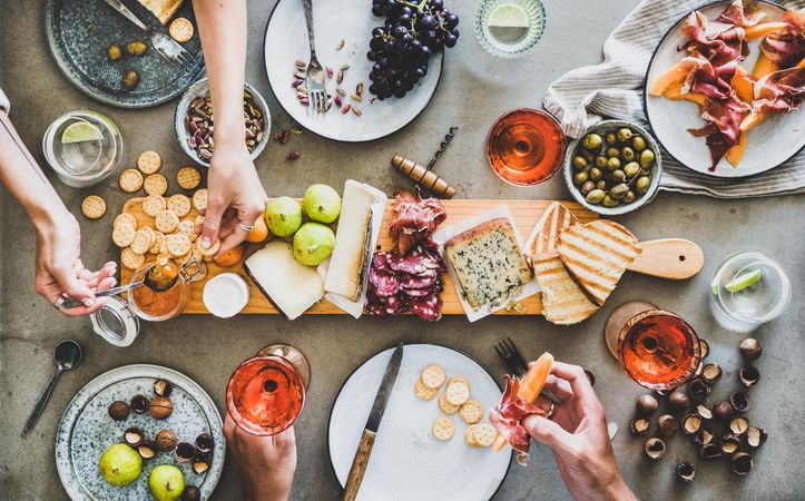 Charcuterie board with hands putting spread on cracker and holding prosciutto and melon