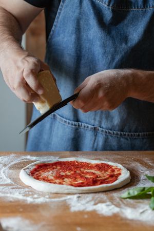 Crop cook grinding cheese on pizza