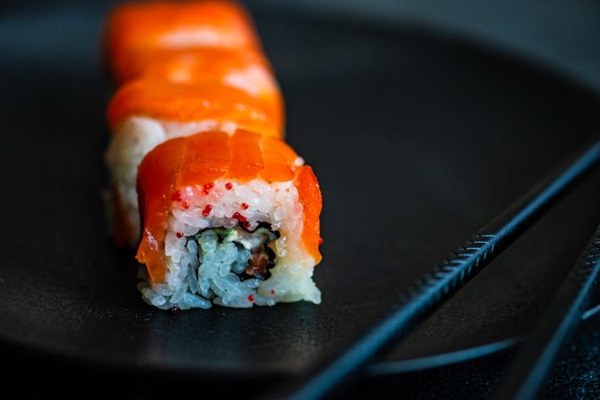 Salmon sushi rolls served on stone slate with chopsticks