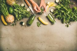 Green smoothie ingredients laying on grey background, with woman with holding smoothie, copy space