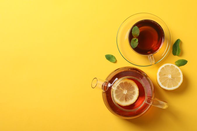 Flat lay. Cup of tea, teapot, lemon and mint on yellow background, copy space
