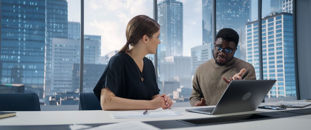 Two Diverse Multiethnic Colleagues Have a Discussion in Bright Skyscraper Office in an Agency.