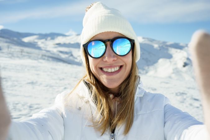 Female in warm clothes beanie cap, and polarized sunglasses smiling and looking at camera
