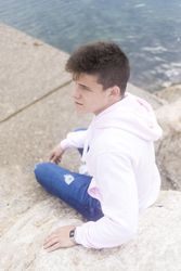 Young pensive teenager male sitting on breakwaters and looking in the distance