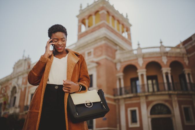 Stylish Black woman with handbag and smartphone on street