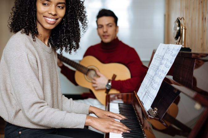 Woman playing piano near man playing guitar in studio