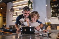 Cheerful father teaching son to cook in kitchen