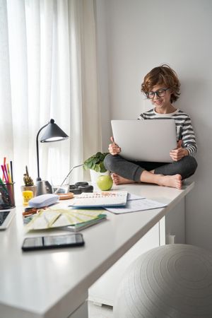Positive curly haired boy with laptop doing homework