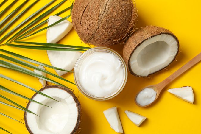 Coconut, cosmetics and palm branch on yellow background, top view